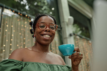 Low angle shot of happy African American woman holding turquoise ceramic cup full of herbal teaの写真素材