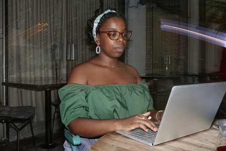 African American woman working remotely via silver laptop in cafeの写真素材