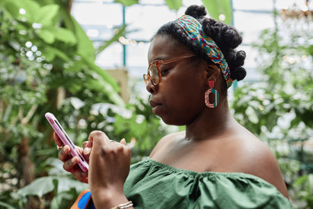 Side view of African American woman using pink smartphone while chilling in eco cafeの写真素材