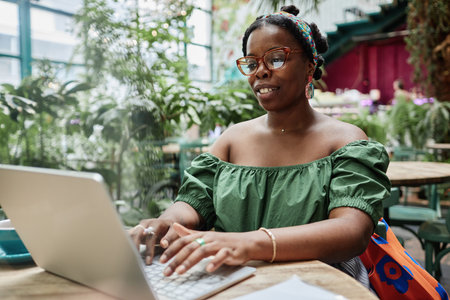 Young African American woman using silver laptop whole chilling in eco cafeの写真素材