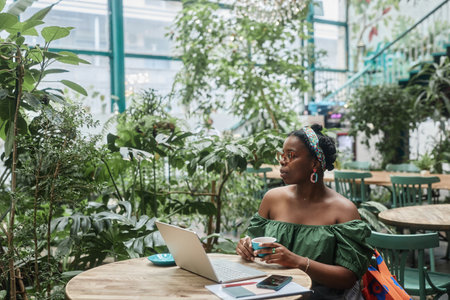 Young African American woman enjoying hot beverage while resting in green cafeの写真素材