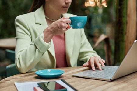 Unrecognizable woman holding turquoise coffee mug and working via laptop in cafeの写真素材