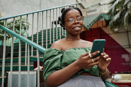 Portrait of young African American woman holding smartphone and looking at cameraの写真素材
