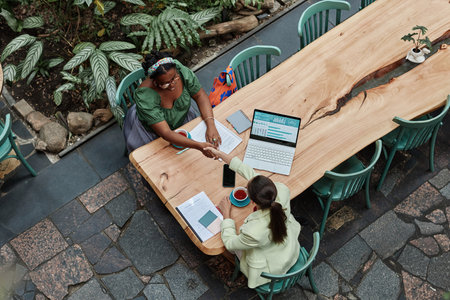 Top down view of two young businesswomen giving handshake to each other during meeting in cozy green cafeの写真素材