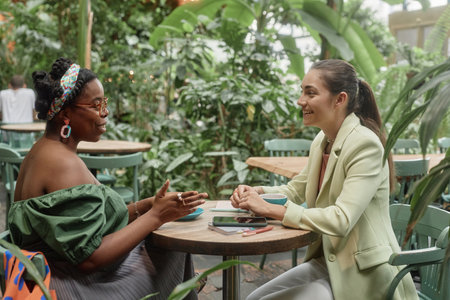 Biracial friends spending free time in eco cafe, they chatting and drinking hot beveragesの写真素材