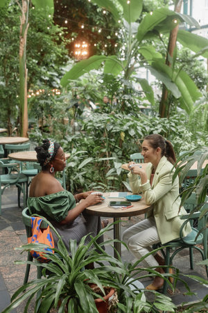 Vertical shot of two besties spending time together in eco cafe full of plants and treesの写真素材