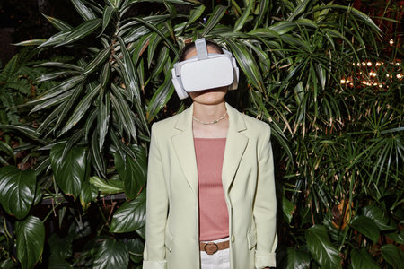 Young woman with white VR set on head posing for photo, verdant plants behind herの写真素材