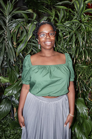 Vertical portrait of smiling African American woman standing near verdant plant wallの写真素材