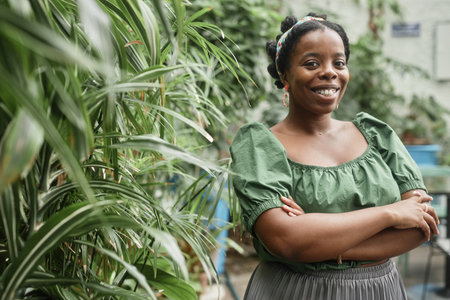 Cute African American woman smiling and posing for portrait, she standing next to green plantsの写真素材