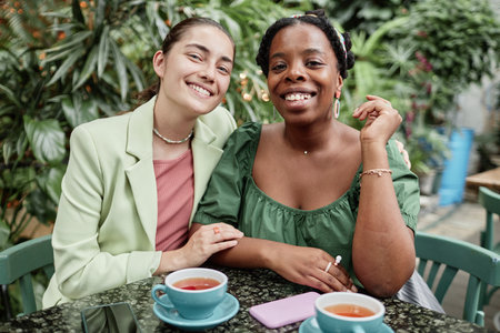 Portrait of happy biracial friends relaxing in cozy eco cafe with huge number of plantsの写真素材