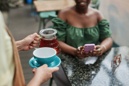 High angle shot of unrecognizable waitress holding teapot and empty turquoise cup while customer sitting at table and waiting for orderの写真素材