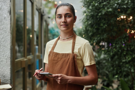 Young Caucasian waitress holding notepad and pen while posing for portrait during her shiftの写真素材
