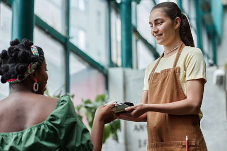 Low angle shot of Caucasian waitress holding payment terminal while unrecognizable customer tapping her cardの写真素材