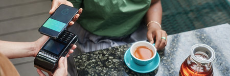 Header of unrecognizable woman sitting at table with beverage and paying via smartphoneの写真素材