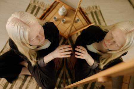 From above view of modern young woman with albinism touching mirror image expressing self-love and self-acceptanceの写真素材