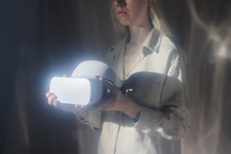 Medium section studio shot of young woman holding futuristic virtual reality headset in her hands