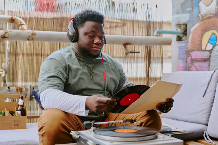 Young man with black headphones on head sitting on terrace sofa and unpacking new vinylの写真素材