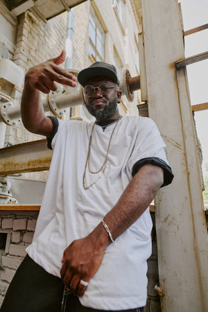 Low angle shot of man with beard dressed in rapper clothes with golden chains showing rap signの写真素材