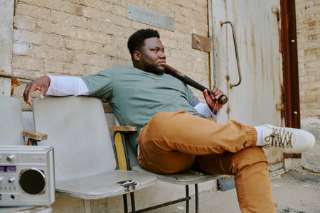Brutal man holding wooden club while sitting on old chair ad listening to tape recorder