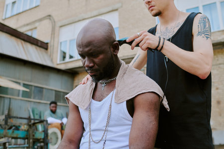 Low angle shot of unrecognizable tattooed male hands shaving head of serious manの写真素材