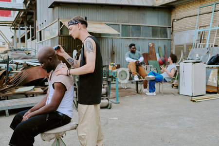 Tattooed dude helping his friend in shaving head while other friends partying in backgroundの写真素材