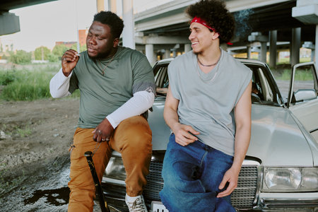 Biracial friends spending time together next to retro car while tough guy smokingの写真素材