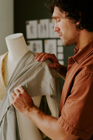 Highly skilled tailor standing next to mannequin and touching light fabric on mannequinの写真素材
