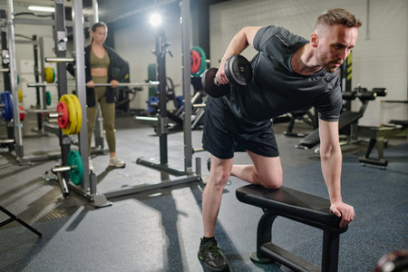 Professional sportsman doing bent over rows while his partner using barbell in blurred backgroundの写真素材