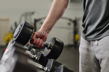 Medium close up of unrecognizable male hand holding heavy rubberized dumbbell