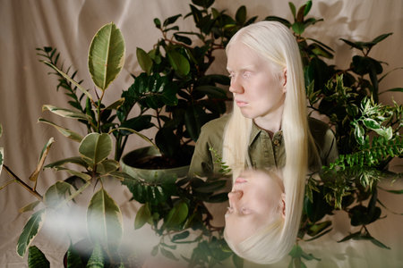 Young woman with albinism and her mirror image in studio decorated with green houseplants, conceptual portraitの写真素材