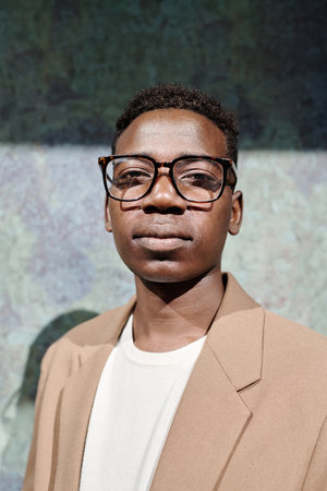 Vertical medium closeup of young African American male CEO wearing eyeglasses standing outdoors and...