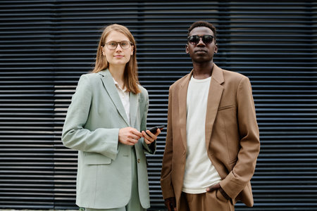 Medium shot of young ethnically diverse gen Z man and woman wearing stylish formal clothes posing for portrait outdoors in business districtの写真素材