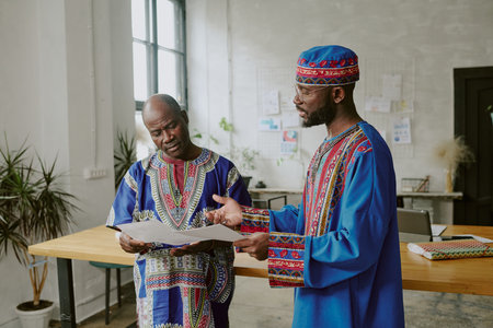 African American coworkers in traditional clothes discussing new startup while working offline in modern officeの写真素材