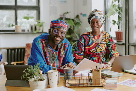 Portrait of smiling African American coworker sitting at wooden table with laptops and documentsの写真素材