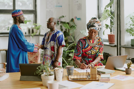 African American female worker writing documents while boss and his subordinate giving handshake to each other in backgroundの写真素材