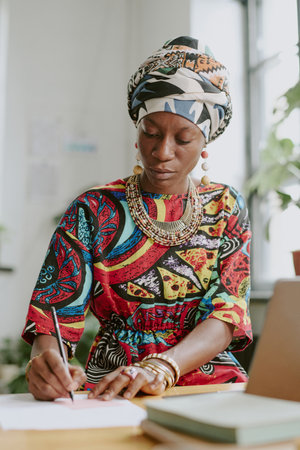 Vertical shot of African American serous woman writing report painstakingly while working offline in officeの写真素材
