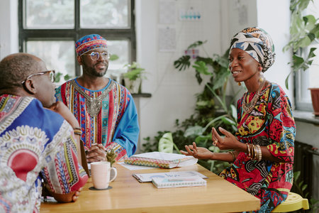 Happy African American woman gesticulating while chatting with her male colleague during coffee brake in officeの写真素材