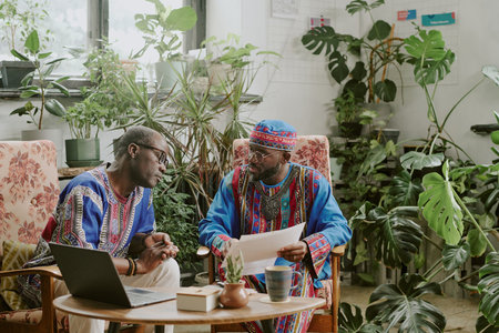 African American coworkers resting on comfortable armchairs and discussing new project during coffee breakの写真素材