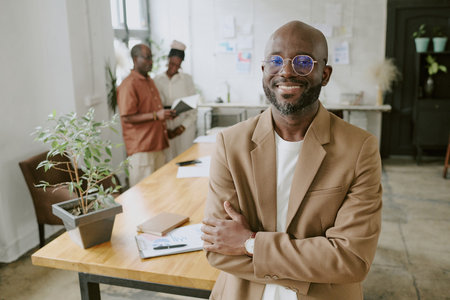 High angle shot of smiling African American businessman posing for photo while his coworkers discussing report in backgroundの写真素材