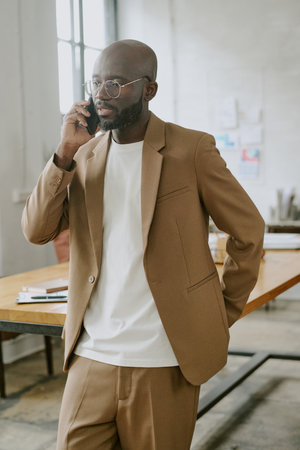 Vertical shot of African American startuper dressed in smart clothes speaking on phone in office