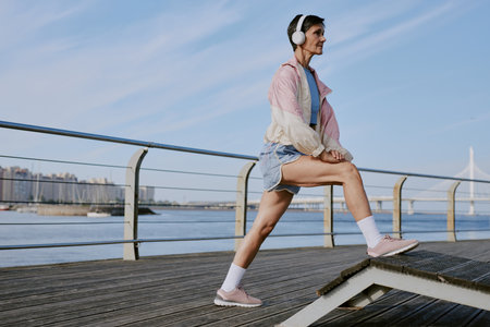 Senior Caucasian woman stretching her leg muscles before jogging on waterfrontの写真素材