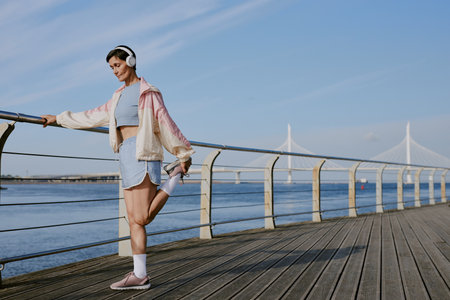 Senior Caucasian woman dressed in pastel colored sportswear warming her knee joint up before jogging on waterfrontの写真素材