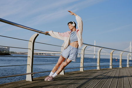 Mature woman enjoying stretching and music on waterfrontの写真素材