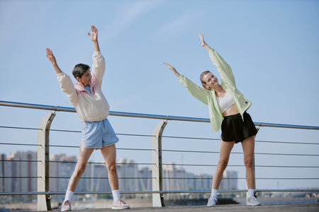Caucasian mom and daughter stretching their bodies, they doing side tilts on waterfront