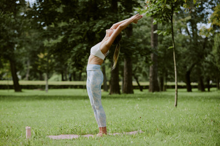 Side view shot of young adult woman standing in Urdhva Hastasana pose on fresh cut lawn in parkの写真素材