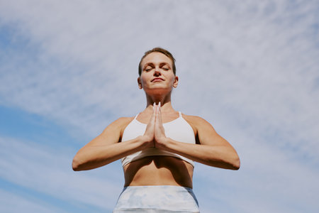 Low angle shot of calm woman in Pranamasana pose under open skyの写真素材