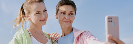 Website banner of senior mom holding her pink smartphone while taking selfie with her adult daughterの写真素材