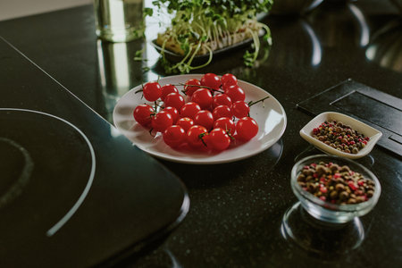 High angle shot of white ceramic plate full of fresh cherry tomatoes, small bowls of spices next to itの写真素材