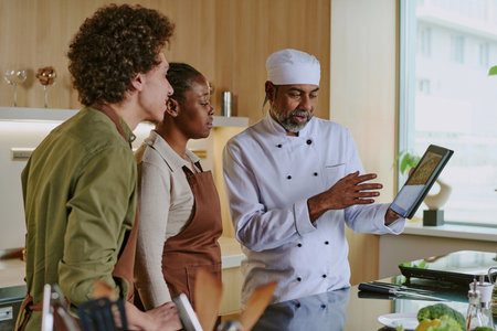 Professional Indian chef showing salad picture from new menu to his young biracial cooksの写真素材