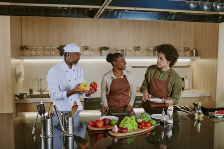 Team of professional chefs of different age choosing ingredients to cook saladの写真素材